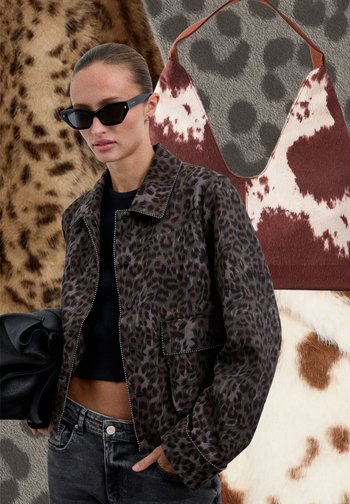 Femeie purtând o geacă întunecată cu imprimeu leopard și ochelari de soare negri, ținând o geantă neagră, cu genți cu imprimeu animalier și fundal din țesătură.