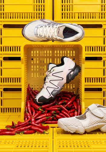 Zapatillas blancas y negras expuestas con pimientos rojos picantes dentro y alrededor de una caja de plástico amarilla.