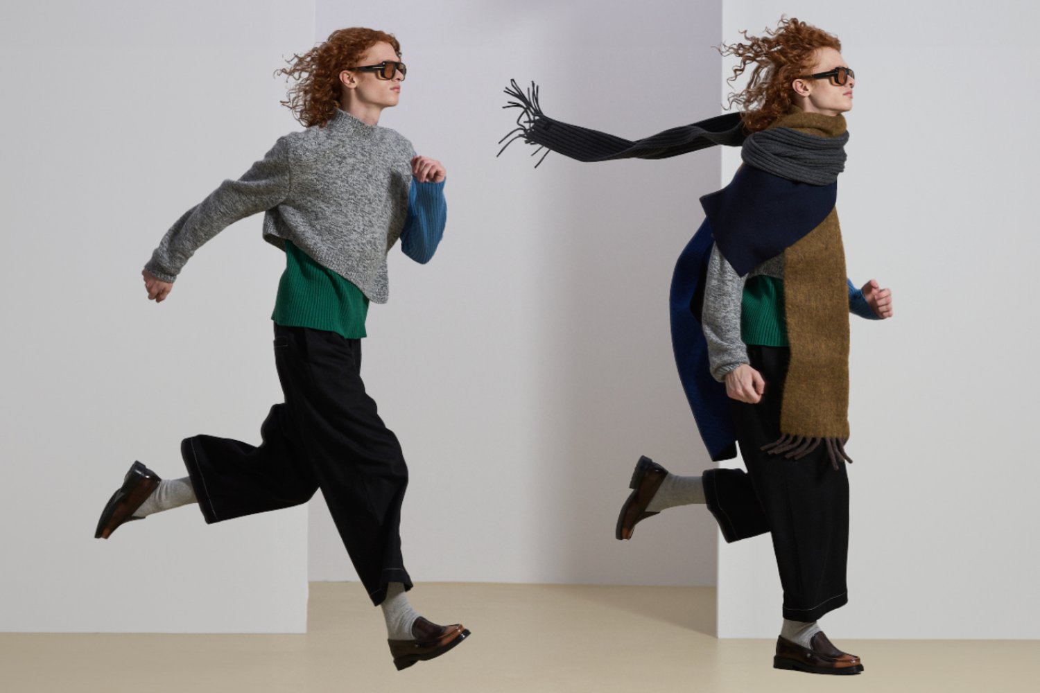 Two models with curly hair, dressed in layered sweaters and scarves, run dynamically against a minimalistic backdrop.