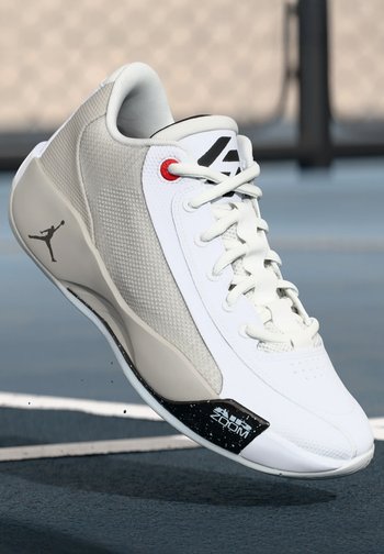 Białe i szare sneakersy wykonane z siateczkowych i skórzanych materiałów, z wyściełanym kołnierzem, czerwonymi akcentami oraz czarną, teksturowaną podeszwą z detalem "Zoom".