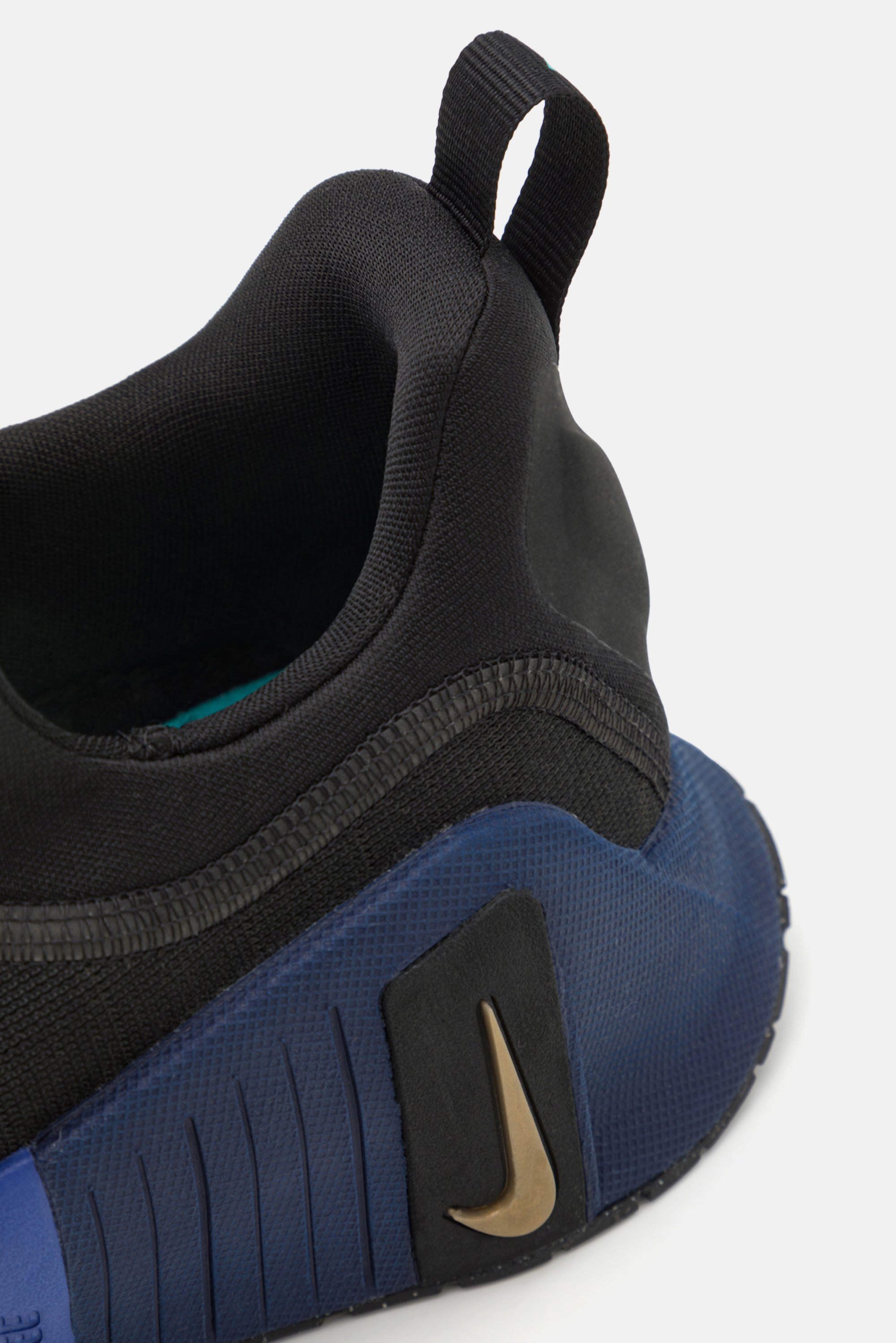 Acercamiento a una zapatilla deportiva negra y azul que muestra un tejido texturizado y un logo dorado de Nike en el lateral, con una lengüeta en el talón.