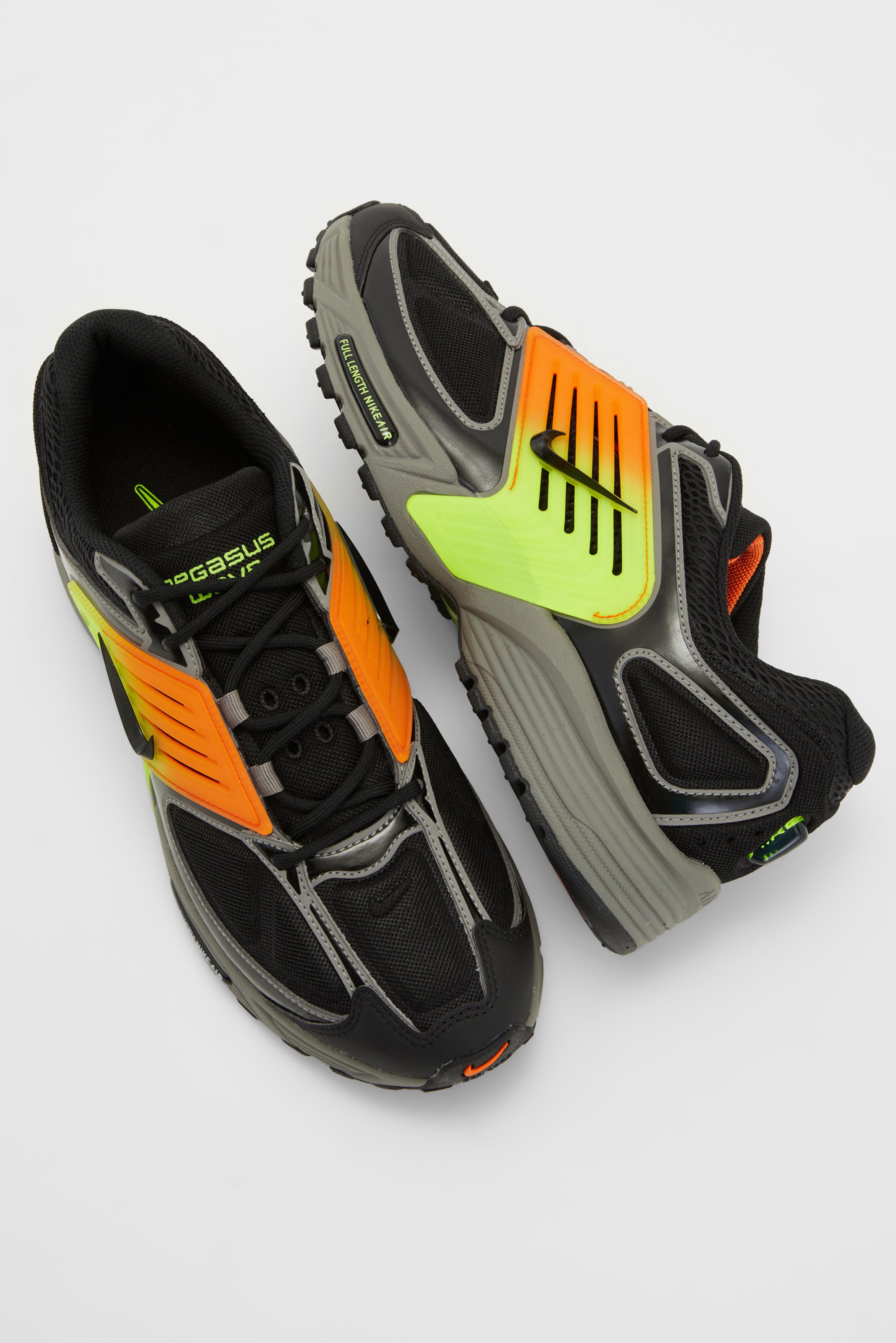 Zwarte en neon hardloopschoenen met grijze accenten en oranje highlights, met een bovenwerk van mesh en een gestructureerde zool, gepositioneerd tegen een witte achtergrond.