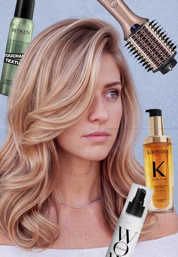 Femme aux longs cheveux blonds et ondulés entourée de produits de soins capillaires comprenant un spray Redken, de l'huile Kerastase, un spray Color Wow et une brosse ronde.