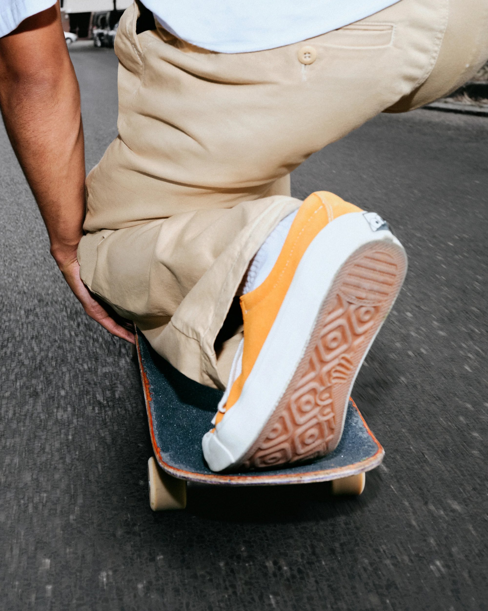 Un primo piano di un piede su uno skateboard, con scarpe arancioni e bianche, mentre scivola lungo un percorso asfaltato liscio.