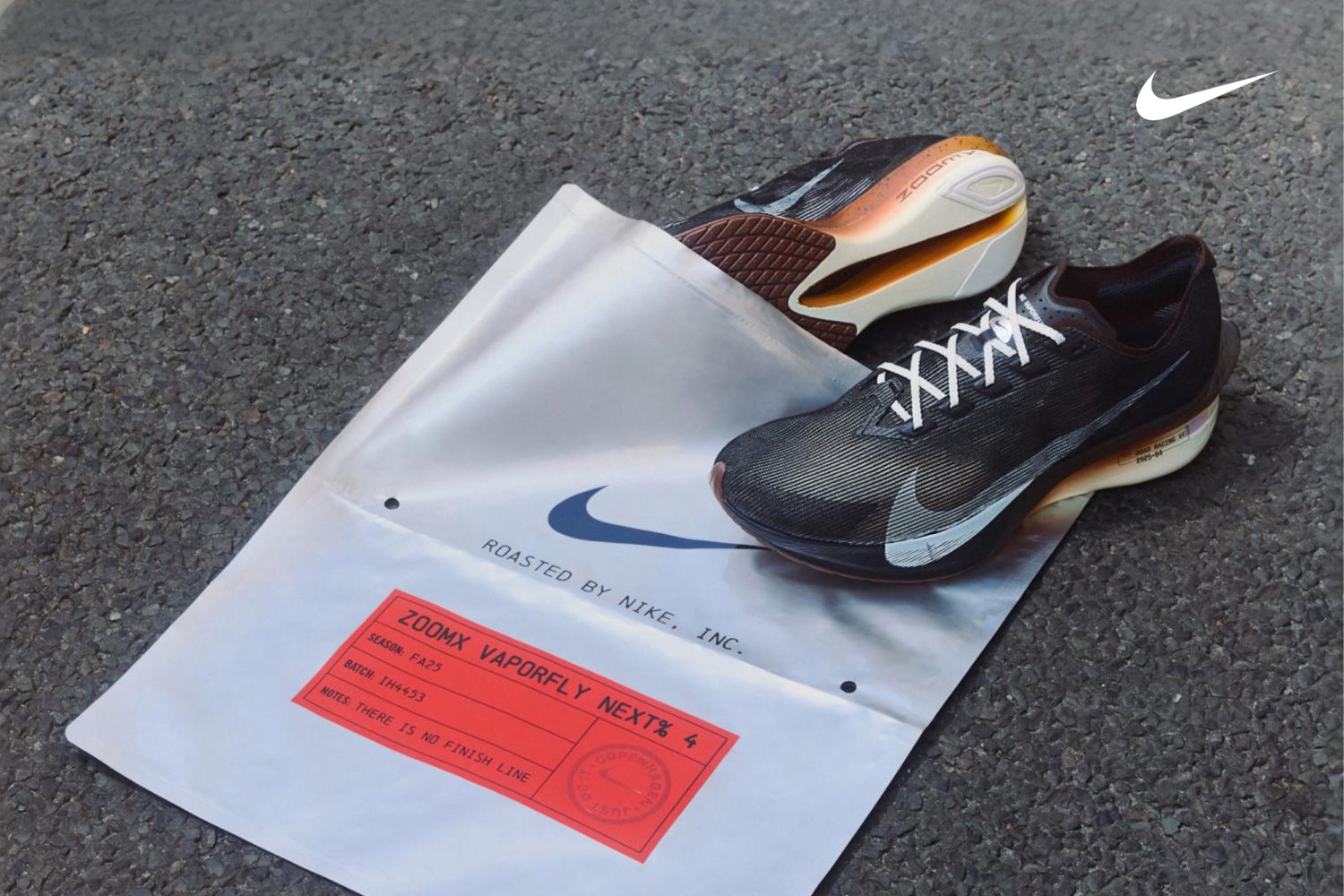 Black and grey Nike ZoomX Vaporfly NEXT% 4 trainers with a textured upper, white laces, and a prominent white swoosh, resting on a branded white bag.