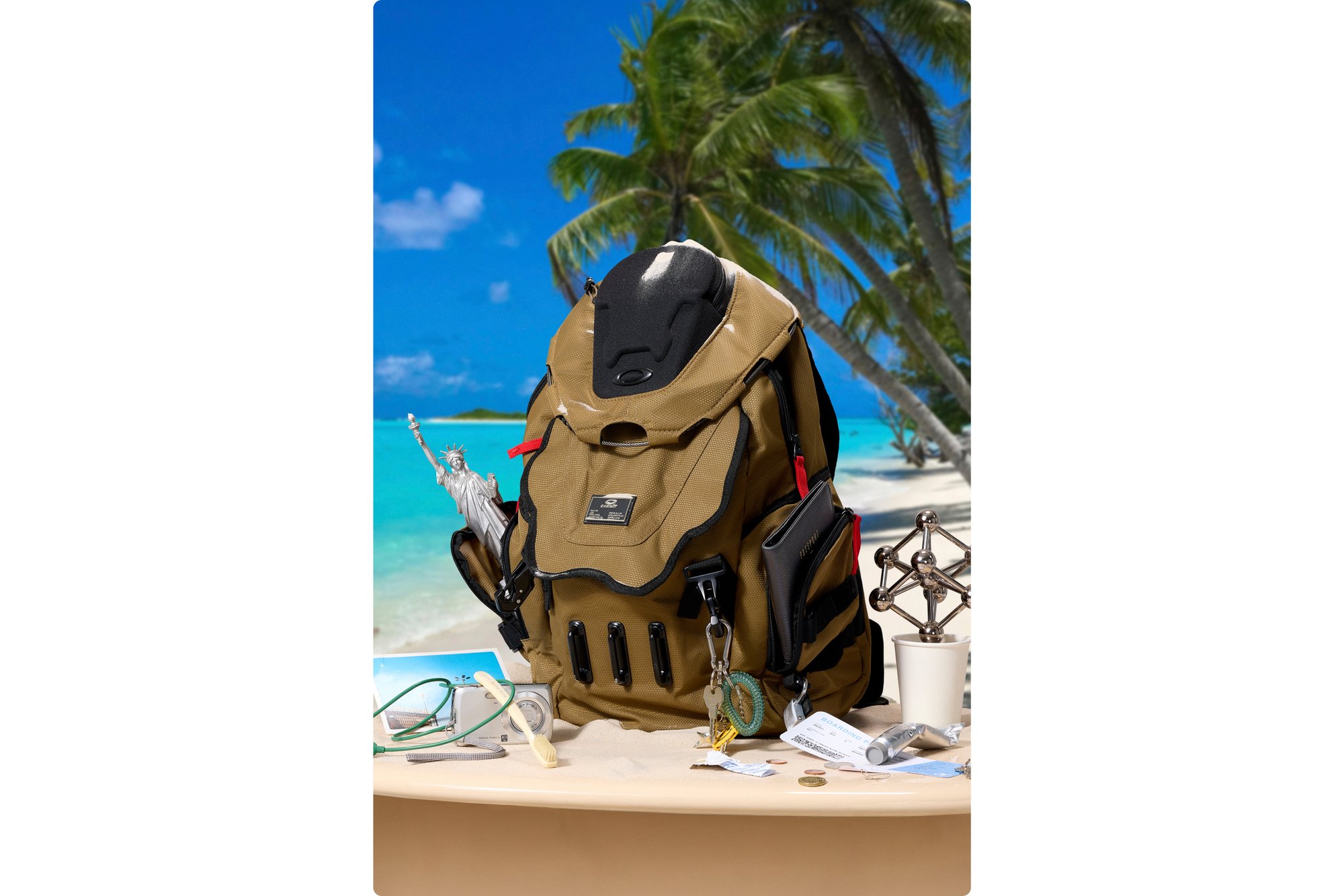 Tan backpack on a table with a beach backdrop; items include sunglasses, a toothbrush, coins, and a small model.