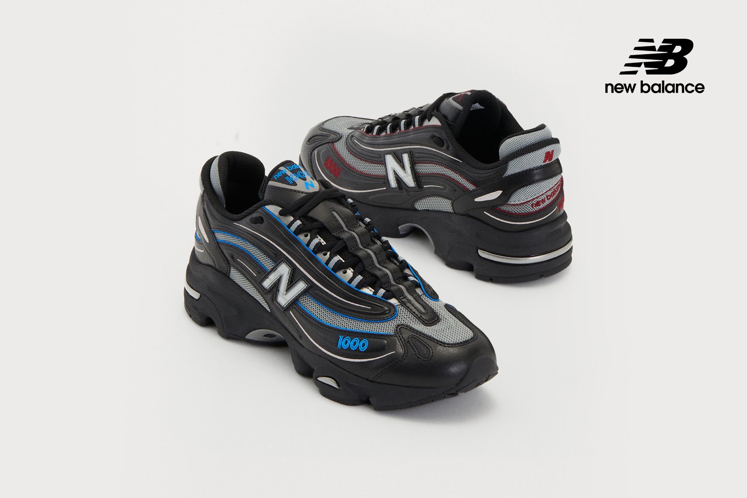 Scarpe da ginnastica nere con accenti blu e rossi, caratterizzate dal logo New Balance e dal numero di modello 1000, esposte su uno sfondo chiaro.