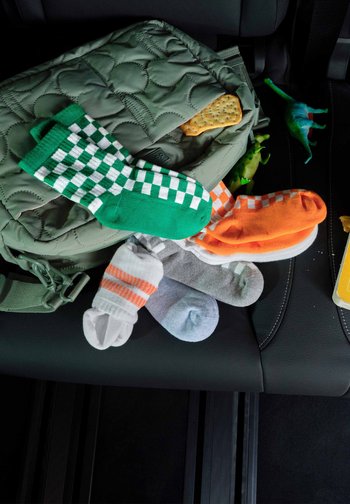 Sac matelassé vert avec des chaussettes à carreaux colorés, des dinosaures jouets et un cracker sur un siège de voiture noir.