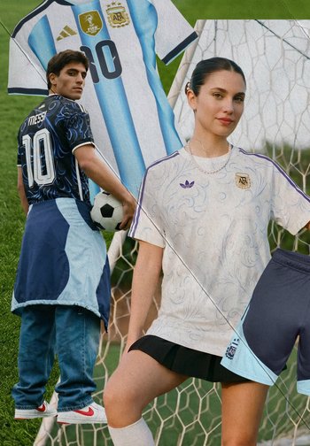 Mann hält einen Fußball mit Messi-Trikot, Frau steht vor dem Tor und trägt ein weißes Argentinien-Fußballtrikot und einen schwarzen Rock.