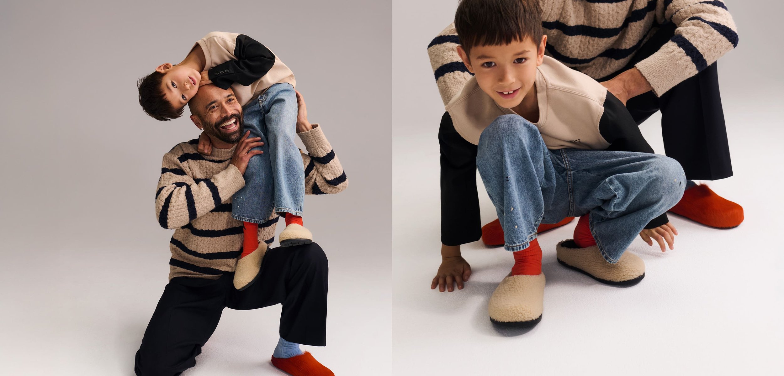 Hombre arrodillado, sonriendo, con un niño sobre sus hombros; el niño inclina la cabeza hacia un lado, lleva jeans azules y zapatillas.