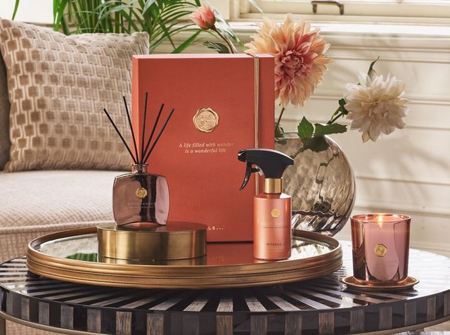 Arrangement of scented products including a diffuser, spray, and candle on a decorative tray, accompanied by flowers in a vase.