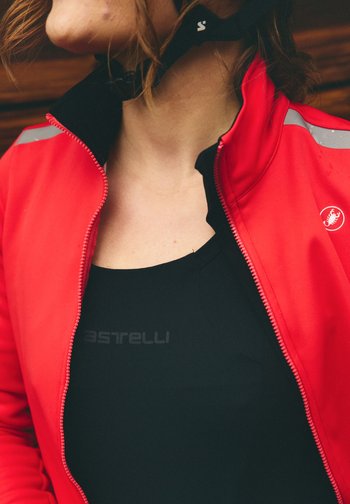 Person som har på seg en rød sykkeljakke, delvis glidelåst over en svart topp med Castelli-logo, med fokus på nakke og øvre brystområde.