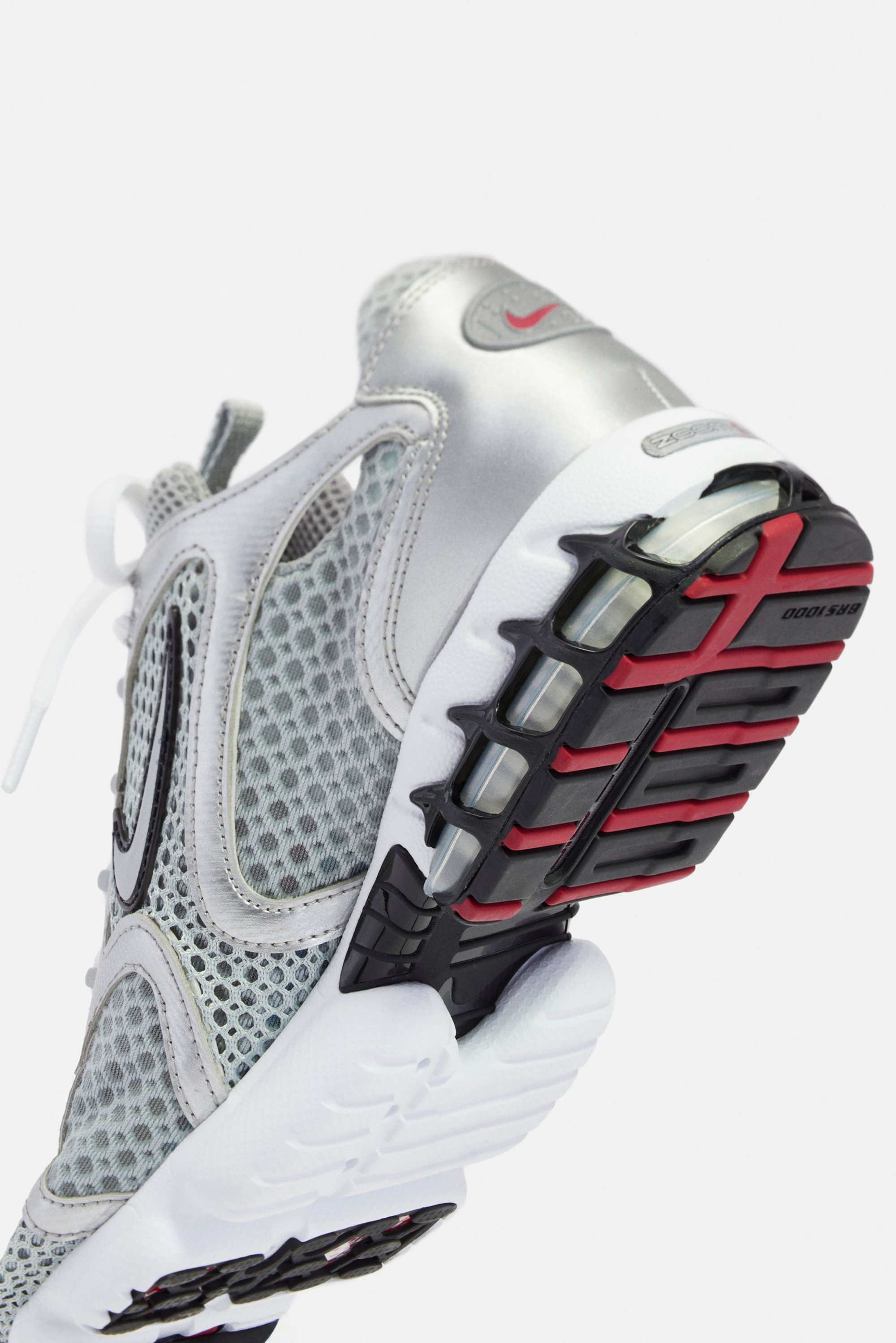 Zilveren en grijze sport schoenen met een bovenkant van mesh, voorzien van een opvallende zwarte en rode buitenzool en een zichtbare luchtkussenunit.