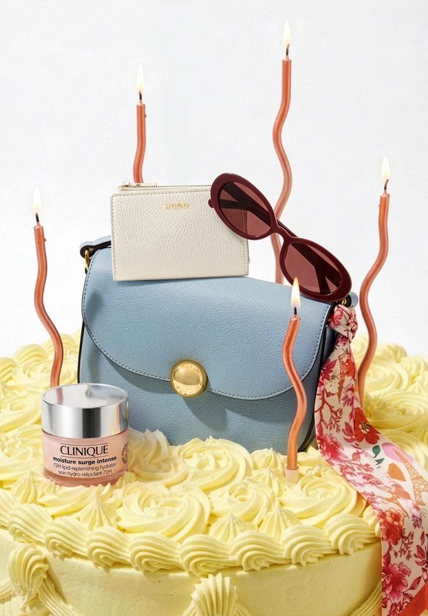 Gelber Kuchen mit Zuckerguss, dekoriert mit einer blauen Handtasche, einem weißen Portemonnaie, roten Sonnenbrillen, einem Blumenhalstuch, Clinique-Feuchtigkeitscreme und fünf brennenden, wellenförmigen Kerzen.