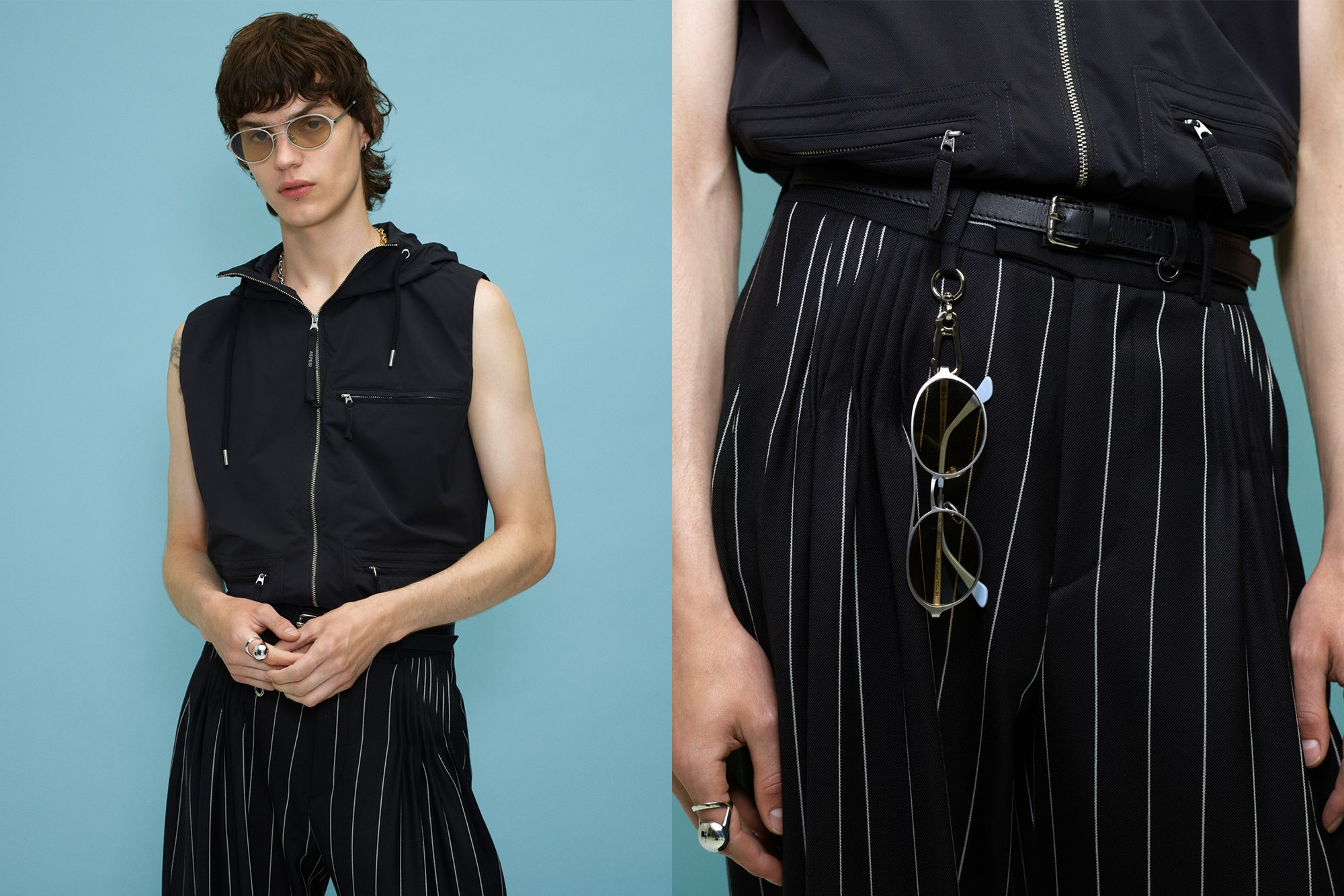 Chaleco negro sin mangas con cremallera y capucha, que presenta cremalleras y bolsillos delanteros; combinado con pantalones negros a rayas y gafas plateadas.