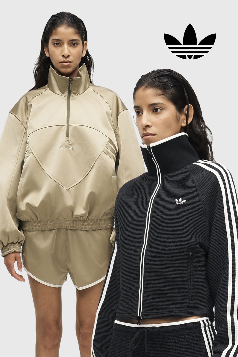 Two women wear Adidas sportswear; one in beige oversized jacket and shorts, the other in black zip-up jacket and pants with white stripes.