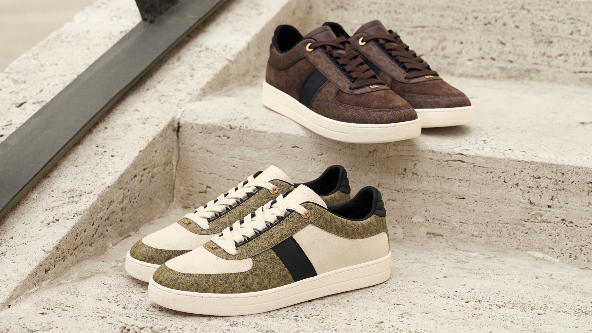 Två par sneakers på betongsteg: ett par i brunt mocka med en svart rand, det andra i krämfärg med grönt geometriskt mönster och svarta detaljer.
