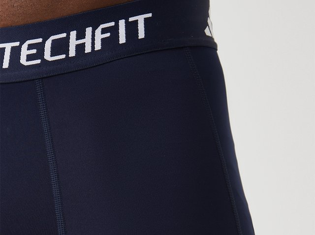 Close-up van marineblauwe sportshorts met elastische tailleband met het label TECHFIT.