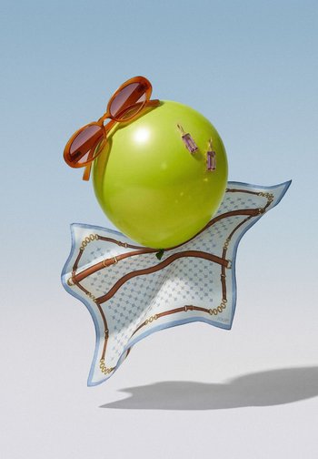 Green balloon wearing brown sunglasses and rectangular purple earrings, resting on a patterned silk scarf against a light blue background.