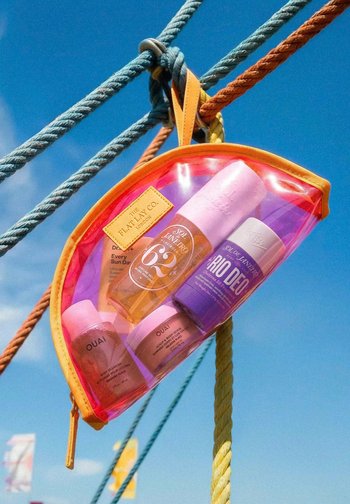 Transparenter rosa und orangefarbener Beutel, der an Seilen hängt und Hautpflege- sowie Deodorantflaschen vor klarem blauem Himmel enthält.