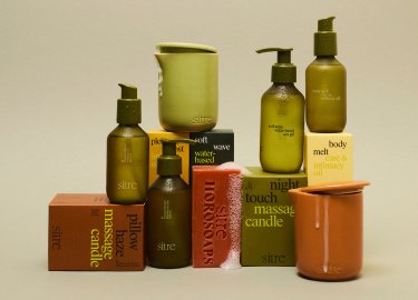 Sześć bursztynowych butelek z pompkami i trzy ceramiczne pojemniki ułożone na oznaczonych pudełkach z produktami do świec do masażu i olejków do ciała.