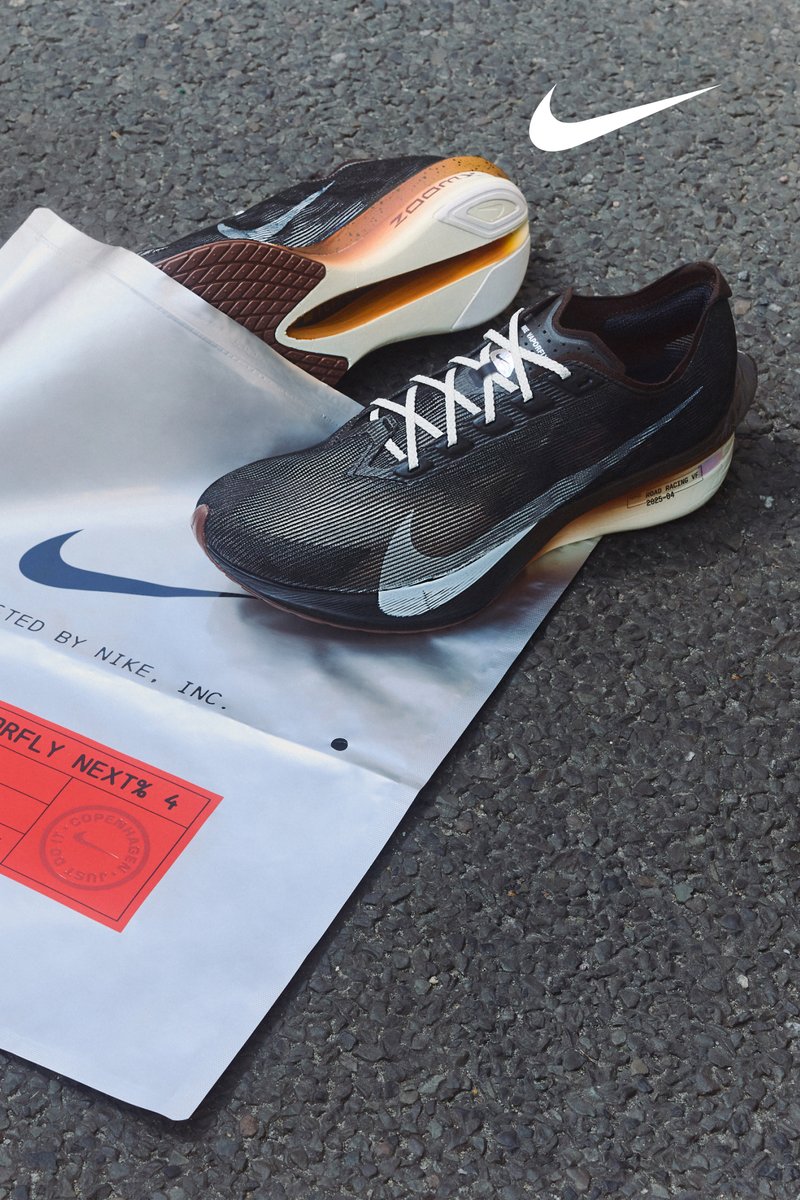 Nike ZoomX-sneakers har en svart ovandel med vita detaljer, inklusive snören och en logo, på en reflexväskan med en röd etikett.