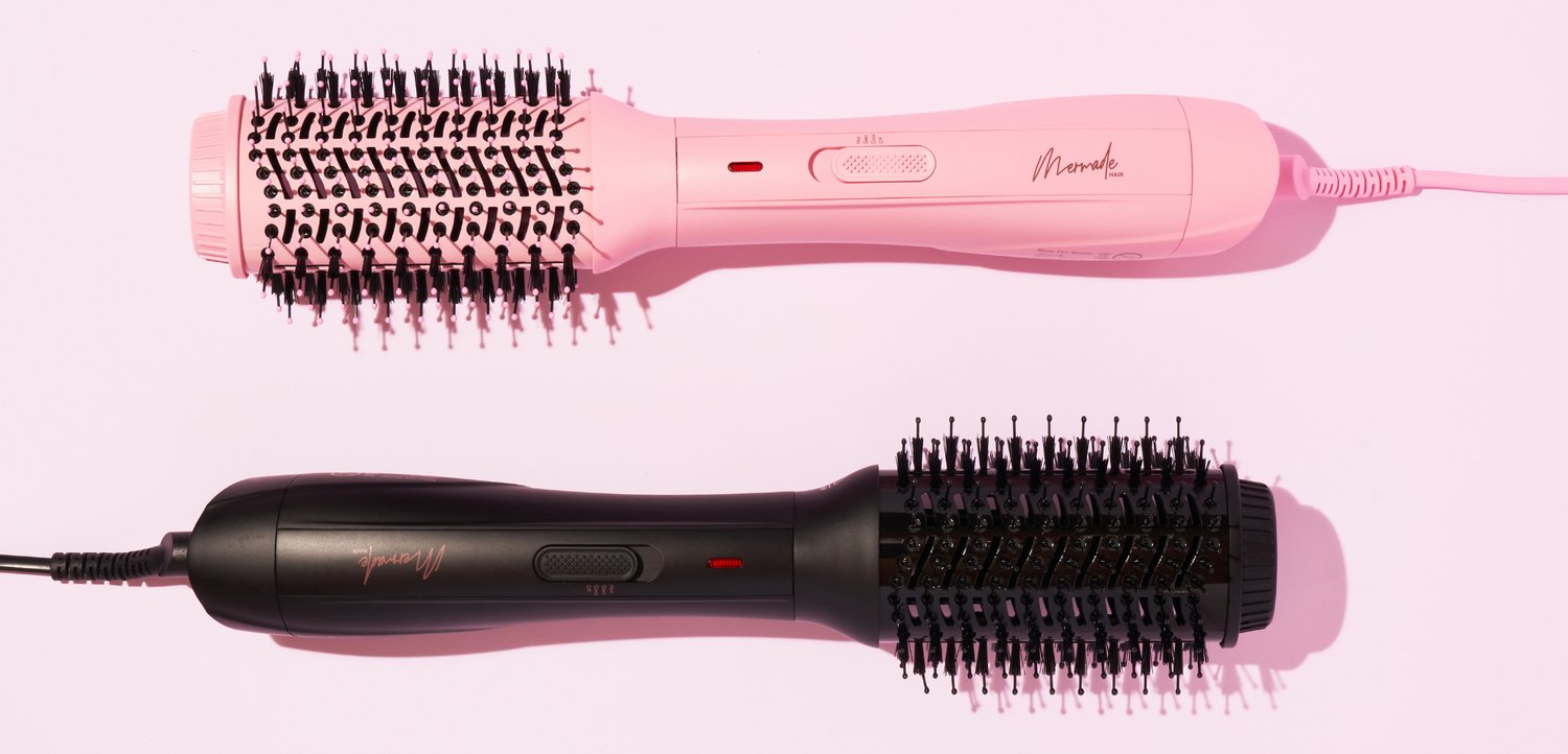 Deux brosses à cheveux électriques rondes, une rose et une noire, placées horizontalement sur une surface rose clair.