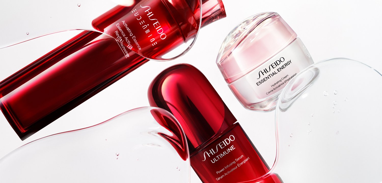 Trzy produkty do pielęgnacji skóry Shiseido w czerwonych i białych opakowaniach na białej powierzchni z kroplami wody wokół nich.