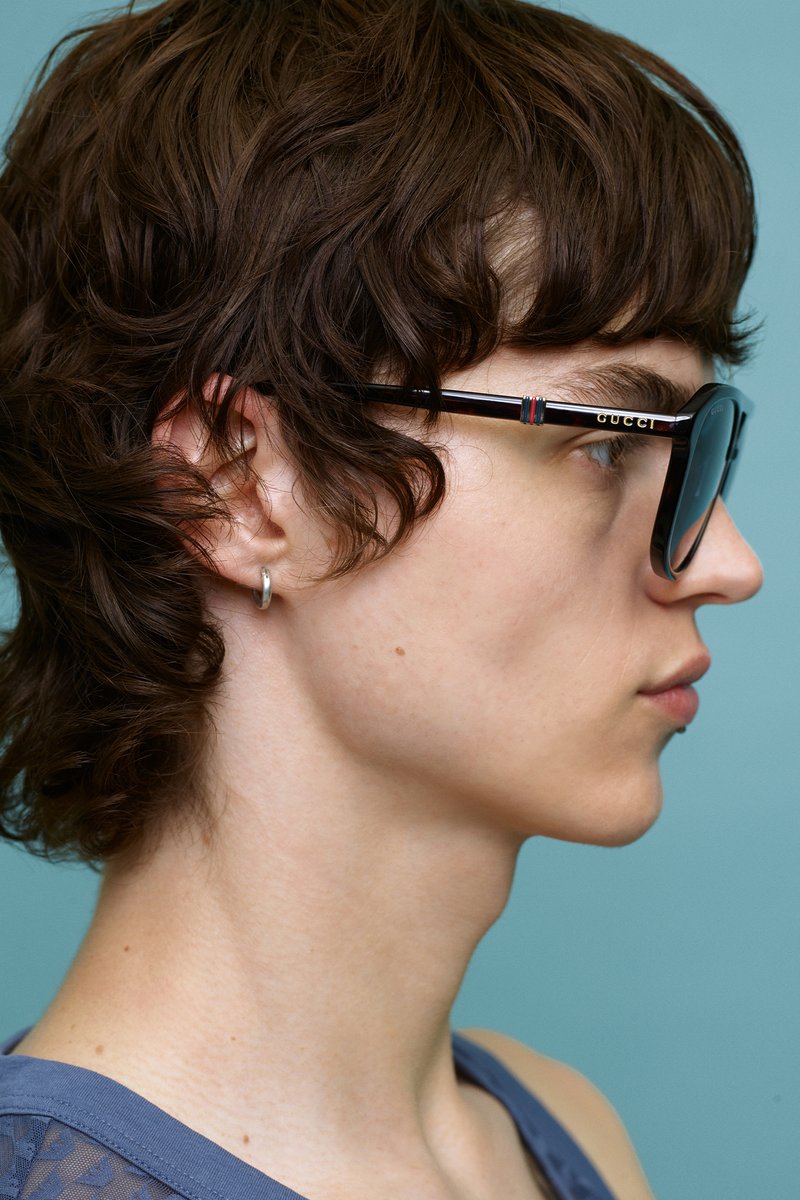 Gafas de sol negras con un acabado brillante, con una franja de color en las patillas, lucidas por una persona con cabello corto y rizado de color marrón.