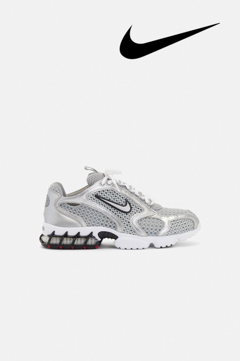 Grijze en witte Nike-sneakers met een mesh-design, met een zwart swoosh-logo, weergegeven op een witte achtergrond.