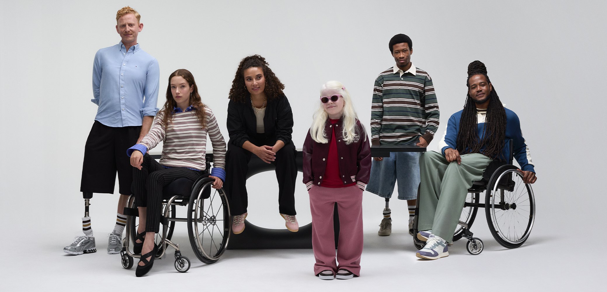 Gruppo di individui diversi, alcuni in sedia a rotelle, che indossano vari outfit casual come magliette a righe, blazer e pantaloni oversize.