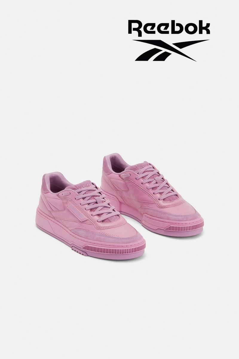 Stylish pink Reebok sneakers with a distinctive design and textured surface, placed against a white background, showcasing the logo above.