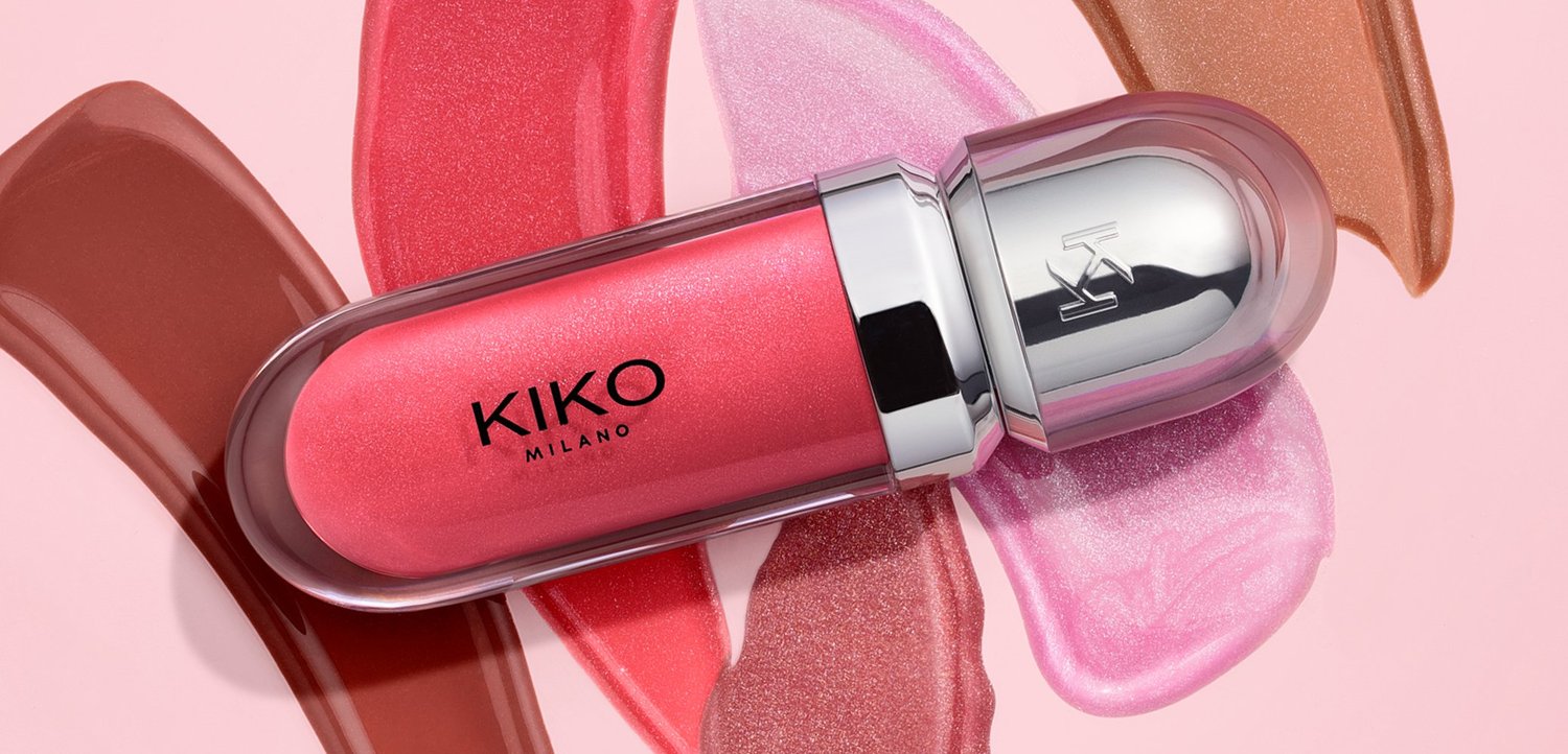 Gloss à lèvres rose Kiko Milano avec un bouchon argenté, posé sur des traces de différentes couleurs de lèvres, notamment marron, corail, rose et tons nude.