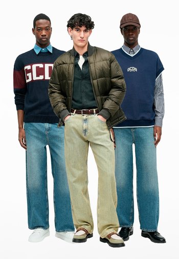 Trois individus se tiennent ensemble. Ils portent différentes tenues : un pull bleu marine, une veste matelassée et un jean en denim large dans différentes teintes.