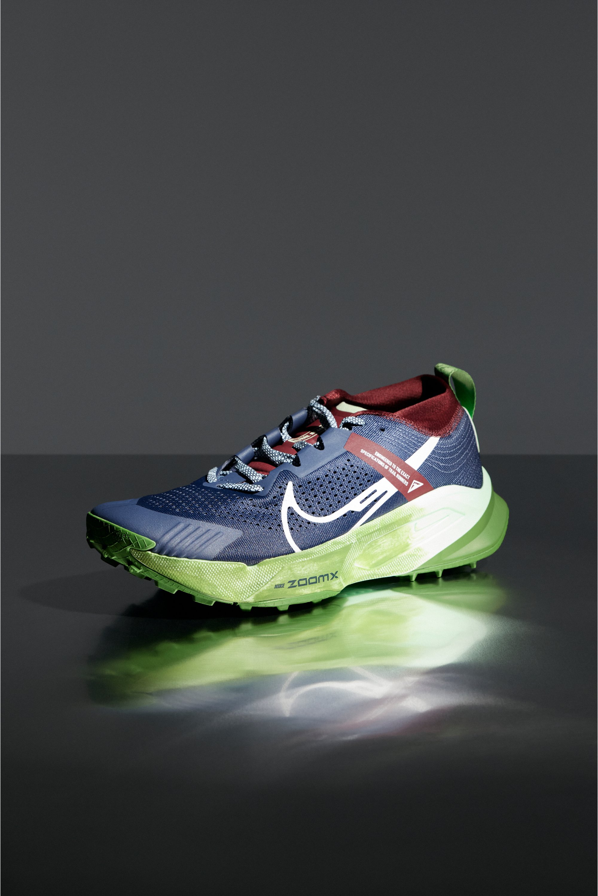 Zapatilla de running en tonos navy y verde con acentos reflectantes sobre una superficie oscura, exhibiendo un diseño elegante y una marca destacada.
