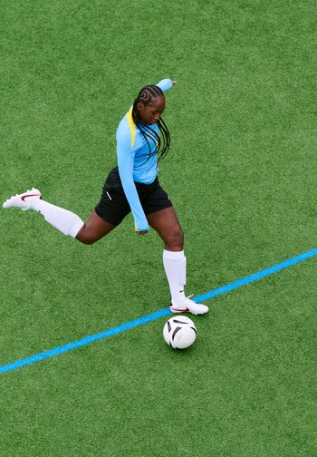 Joueuse de football en maillot bleu et chaussettes blanches frappant le ballon sur un terrain vert près d'une ligne bleue.