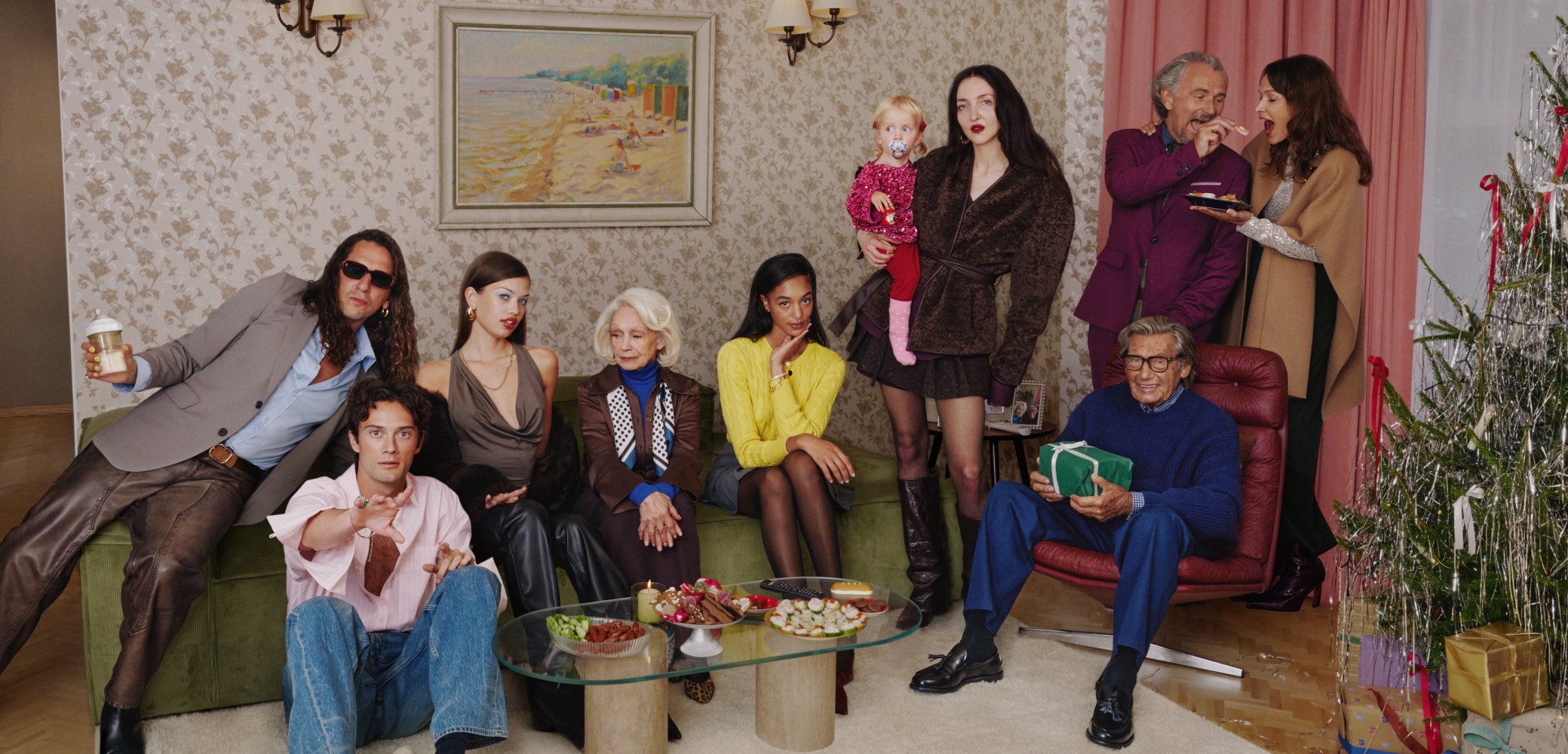Gruppe av mennesker i en koselig innendørs setting. Varierte klesstiler, farger og teksturer; har en grønn sofa, glassbord med snacks, og et dekorert juletre.
