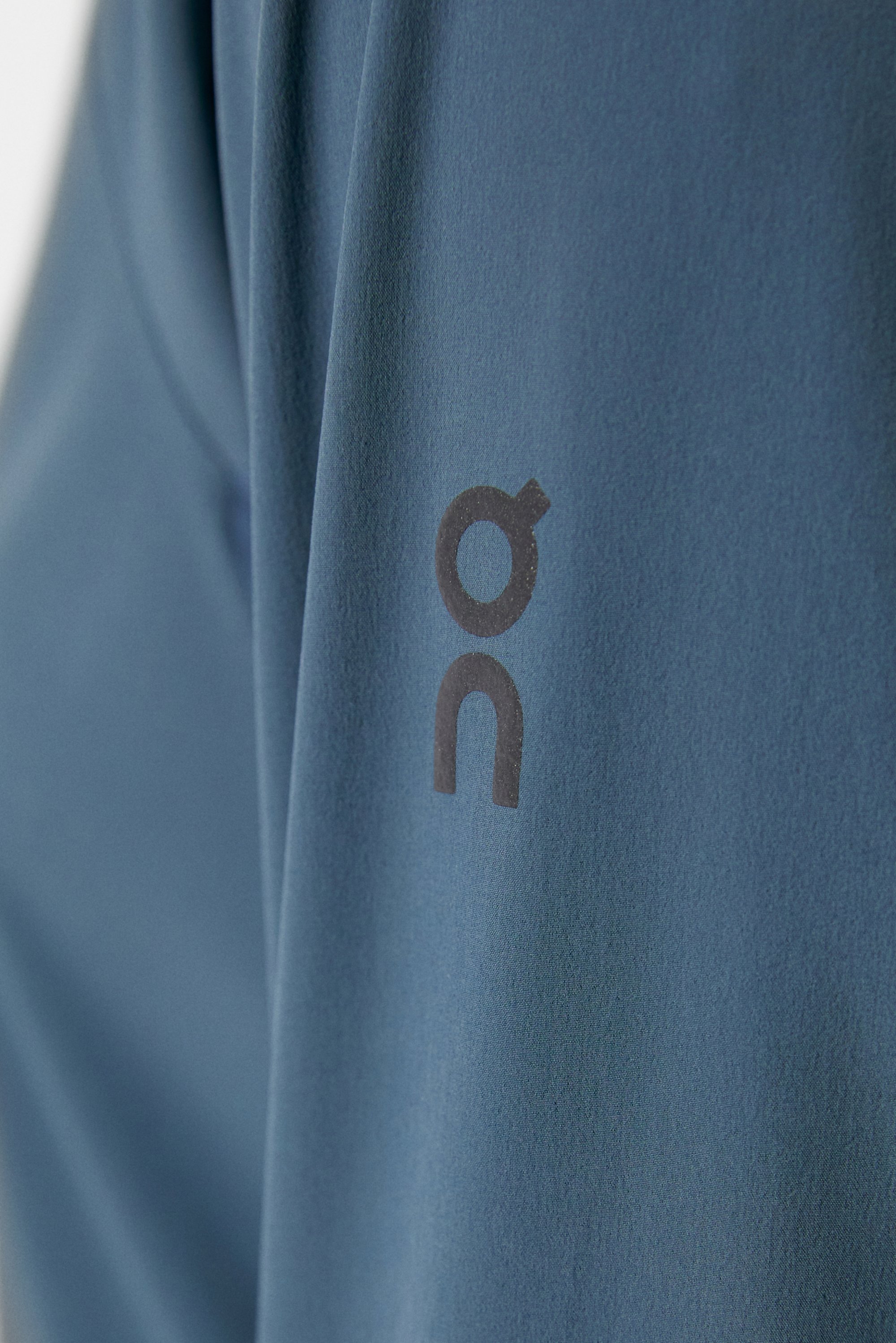 Close-up of a blue shirt featuring a prominent dark logo that reads "on" on the sleeve, highlighting fabric texture and design.