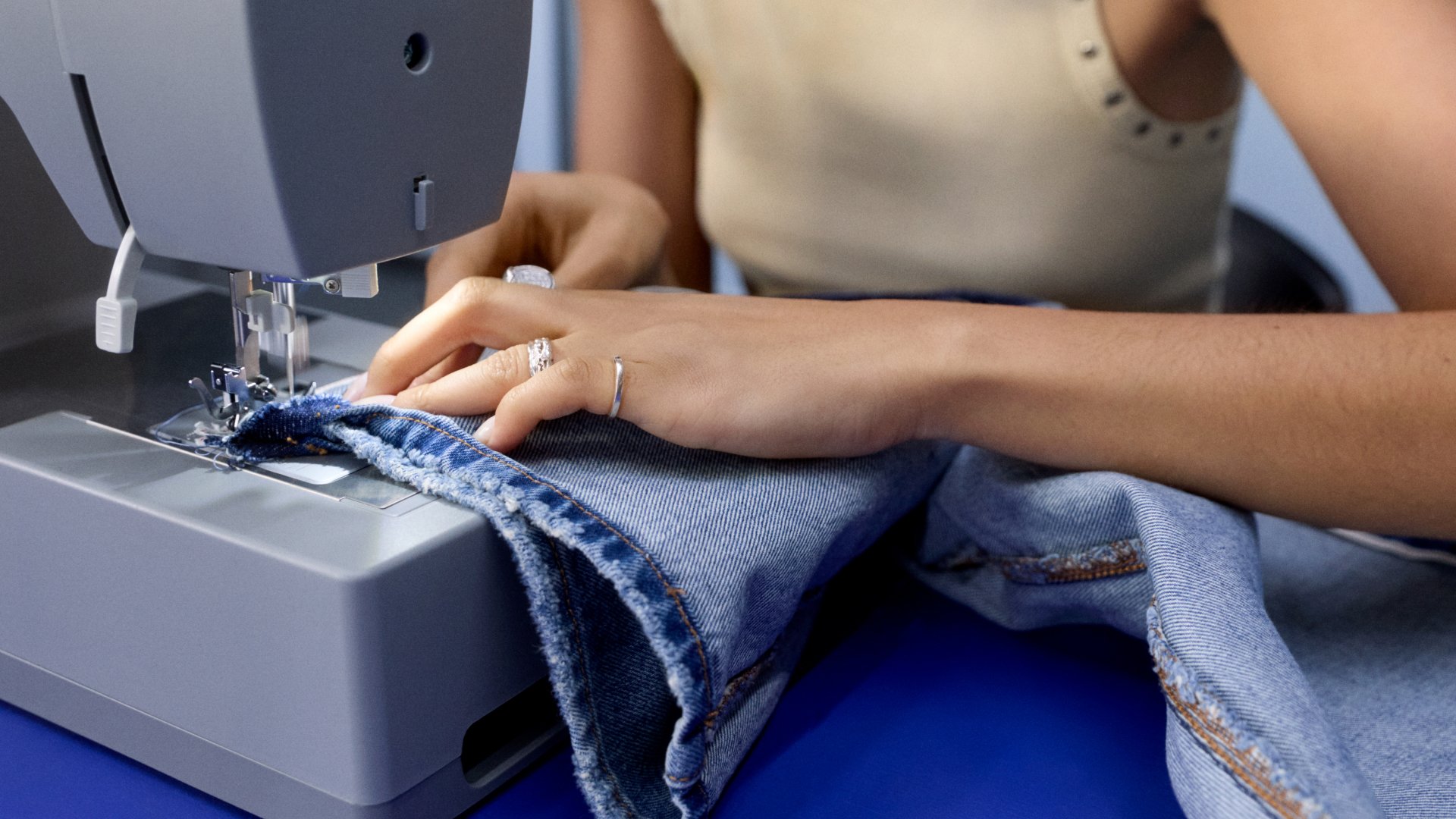 Een persoon leidt zorgvuldig denimstof onder de naald van een naaimachine, geconcentreerd op het naaien van een naad, met handen versierd met ringen.