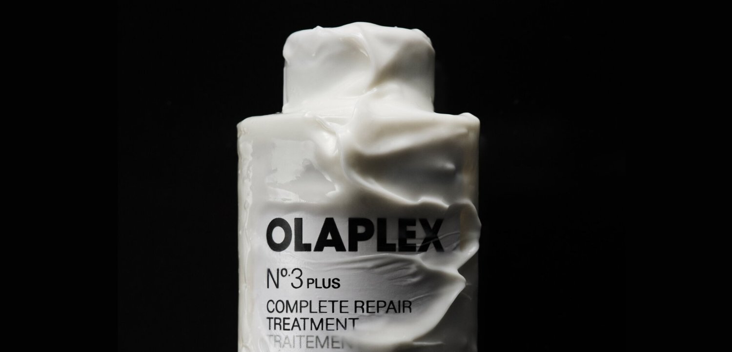 Olaplex No. 3 Plus Complete Repair Treatment Flasche, bedeckt mit weißem cremigem Produkt vor schwarzem Hintergrund.