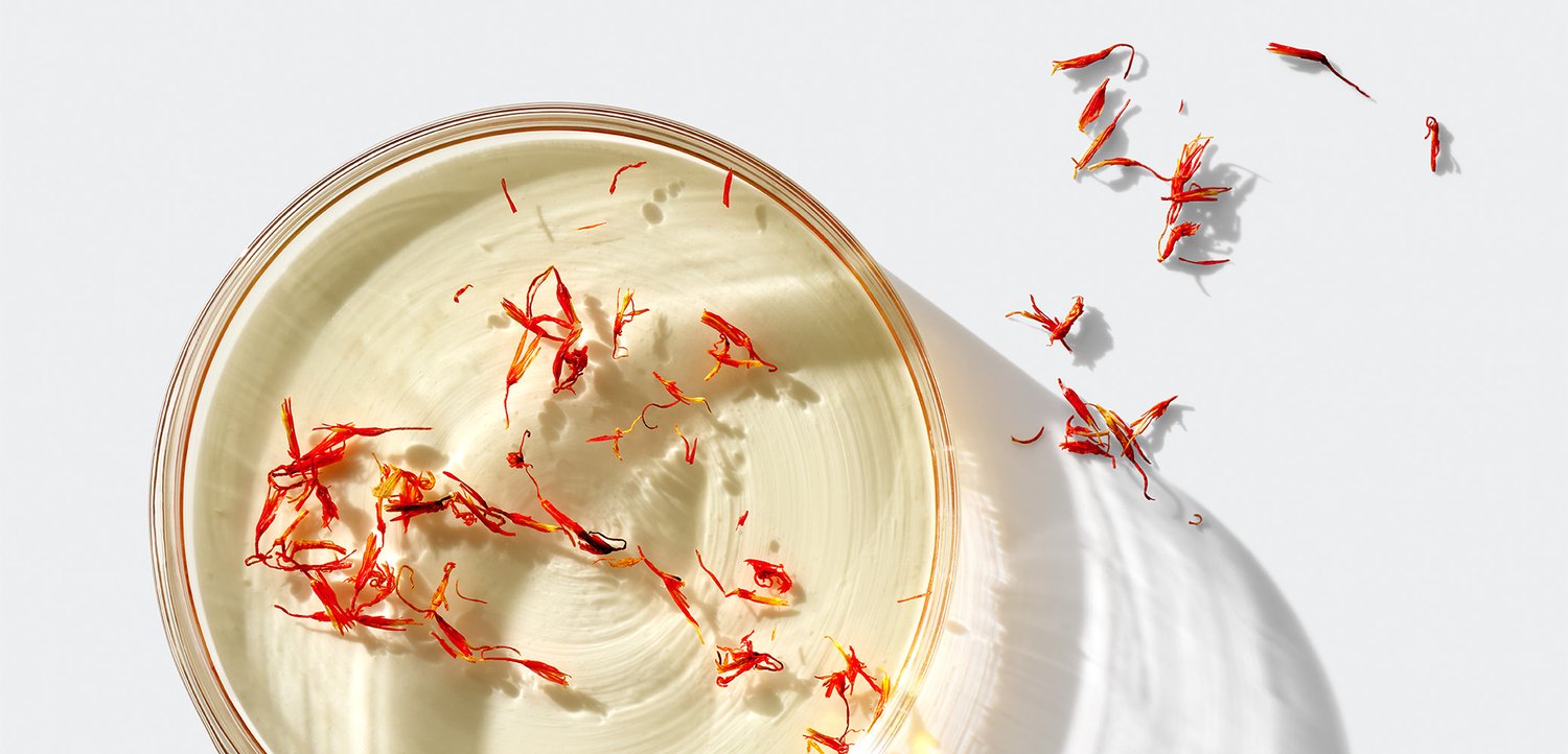 Cremiger weißer Dip in einer flachen Glasschale, garniert mit leuchtend roten Safranfäden, mit verstreuten Safranakzenten auf hellem Hintergrund.