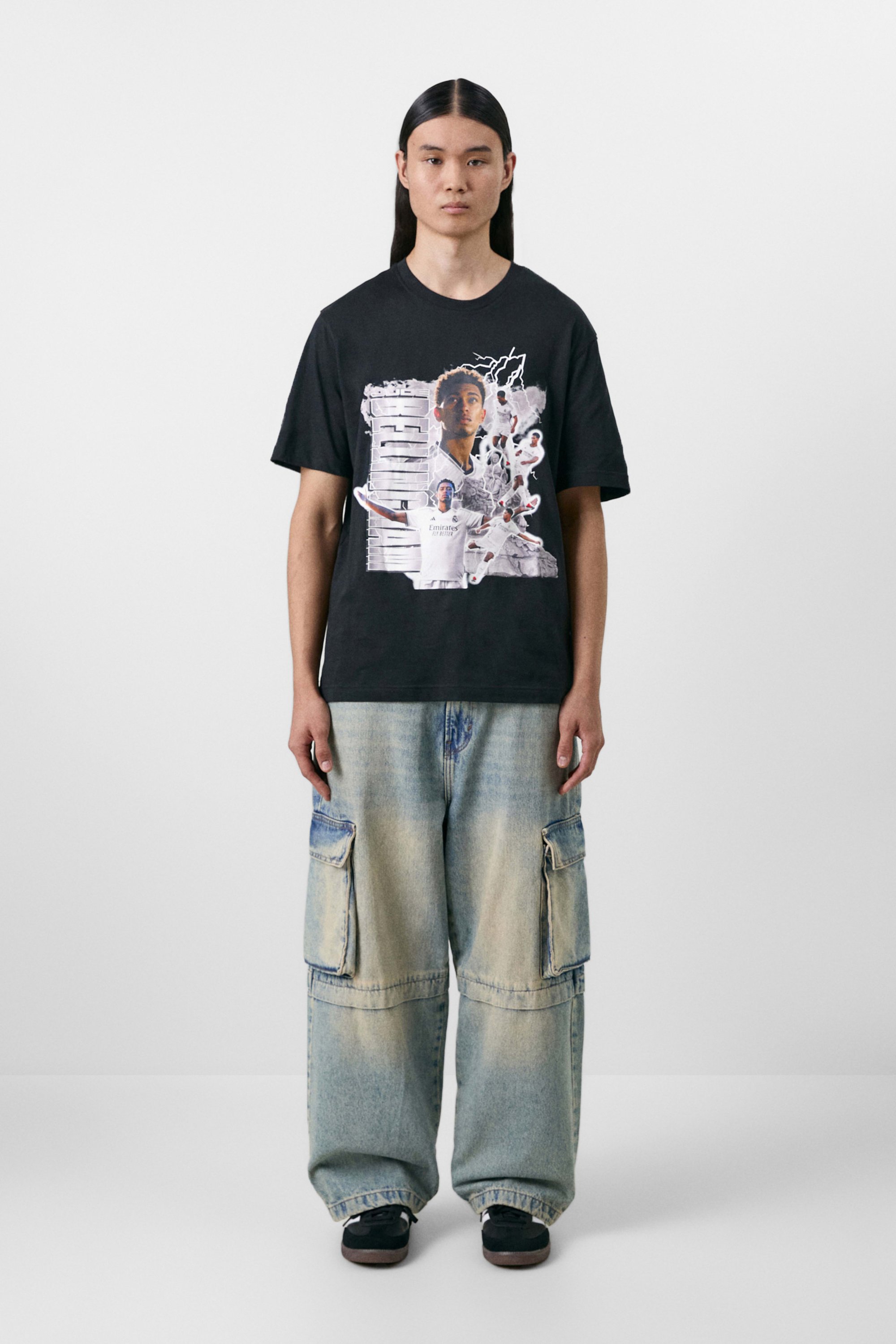 Camiseta de algodón negra con un diseño gráfico multicolor, combinada con unos pantalones cargo azules desgastados y holgados con múltiples bolsillos. Zapatillas negras.
