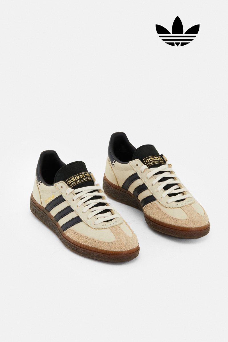Sneaker Adidas beige con strisce e lacci neri, dotate di suola in gomma e un piccolo logo sul lato, esposte su uno sfondo bianco.