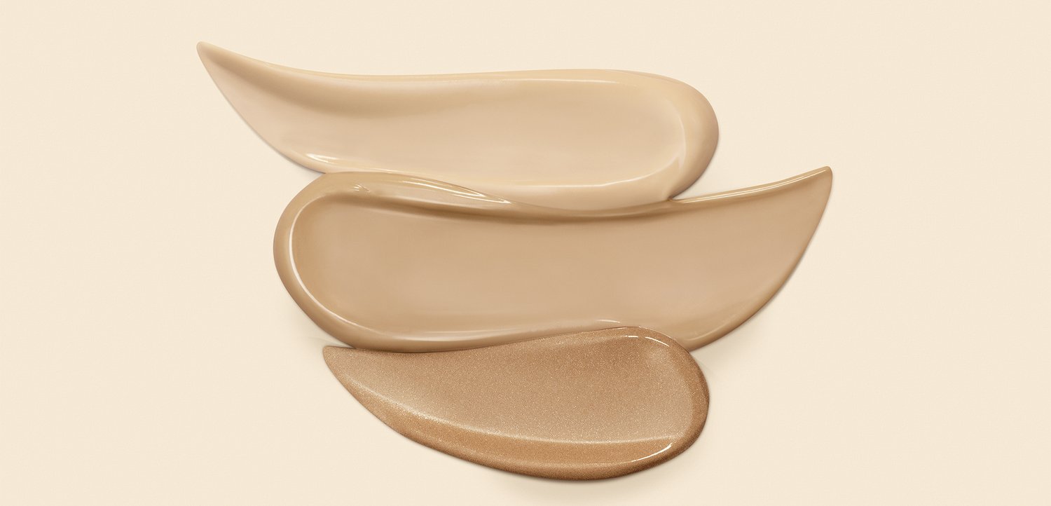 Tre glatte, aflange foundationprøver i forskellige beige toner lagdelt på en lys baggrund.