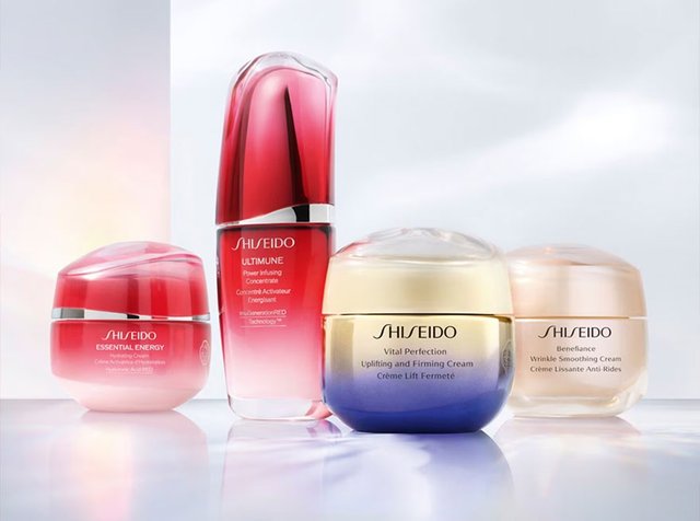 Cuatro productos de cuidado de la piel de Shiseido en diferentes envases: suero rojo y tarros de crema en tonos blanco, dorado y rosa, todos organizados de manera elegante.