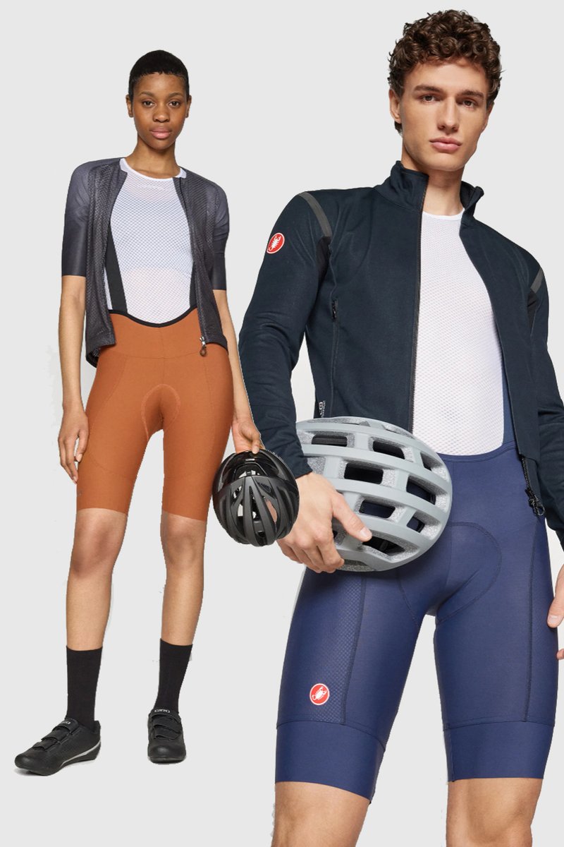 Two cyclists showcase athletic wear: a woman in a black and orange outfit, and a man in navy shorts, holding a black and gray helmet.