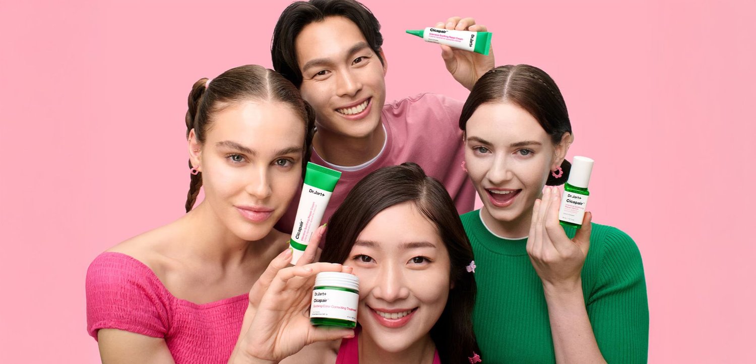 Vijf huidverzorgingsproducten van Dr. Jart+ worden getoond door vier personen tegen een roze achtergrond. Producten in groene en witte verpakking omvatten crèmes en serums.