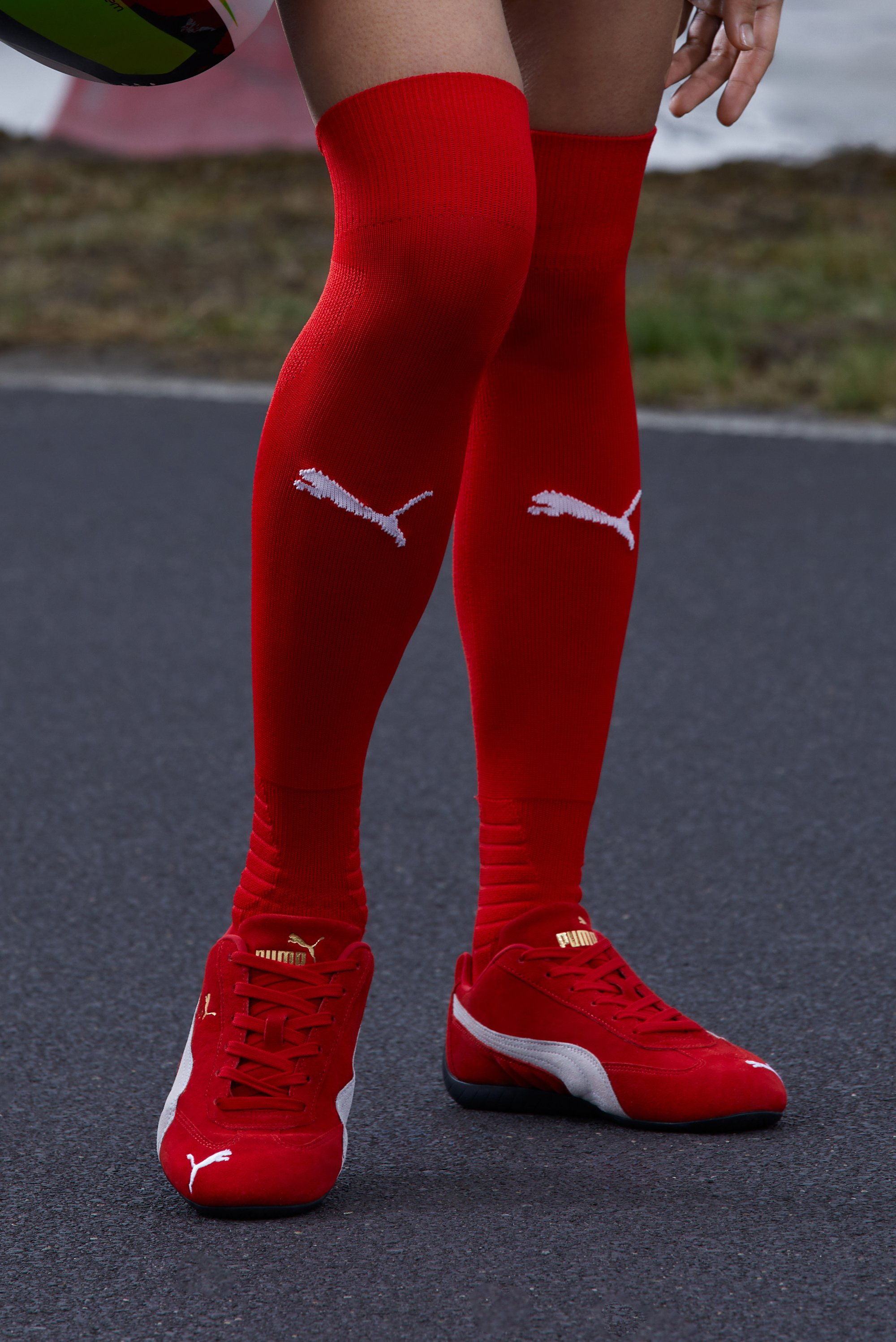Rode kniekousen en bijpassende rode sportjeuken worden gedragen op de benen van een persoon, die staat op een verharde baan met groen achtergrond.