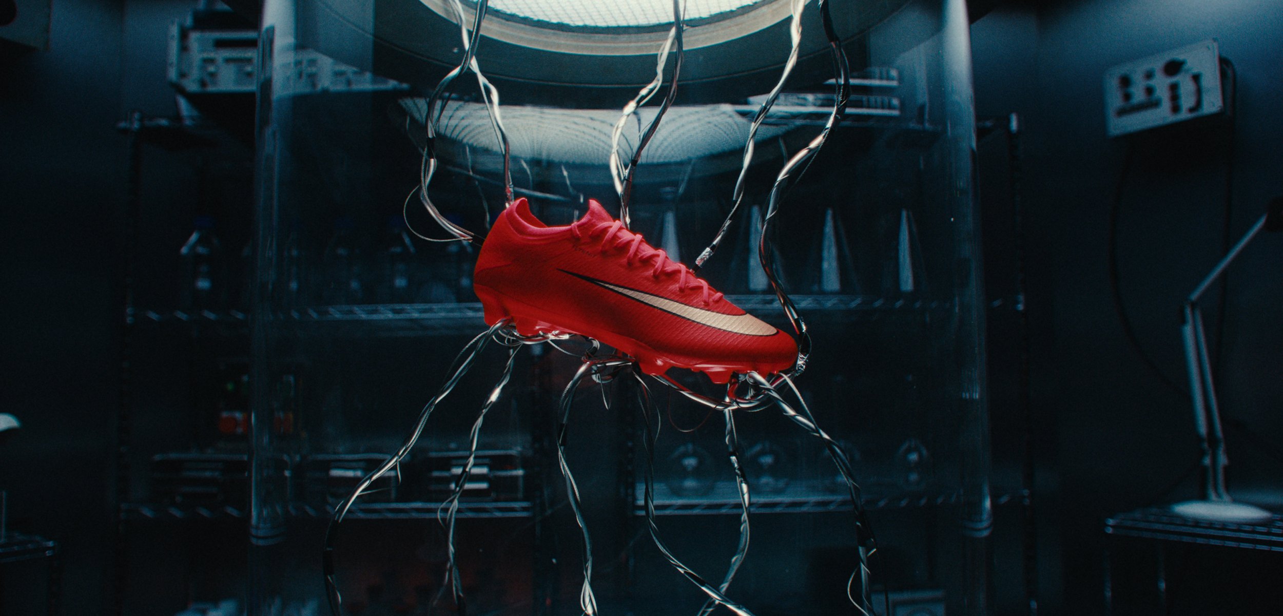 Roter Fußballschuh, der in einem dunklen Labor aufgehängt ist, verbunden mit mehreren leuchtenden Kabeln, mit Industrieausrüstung im Hintergrund.