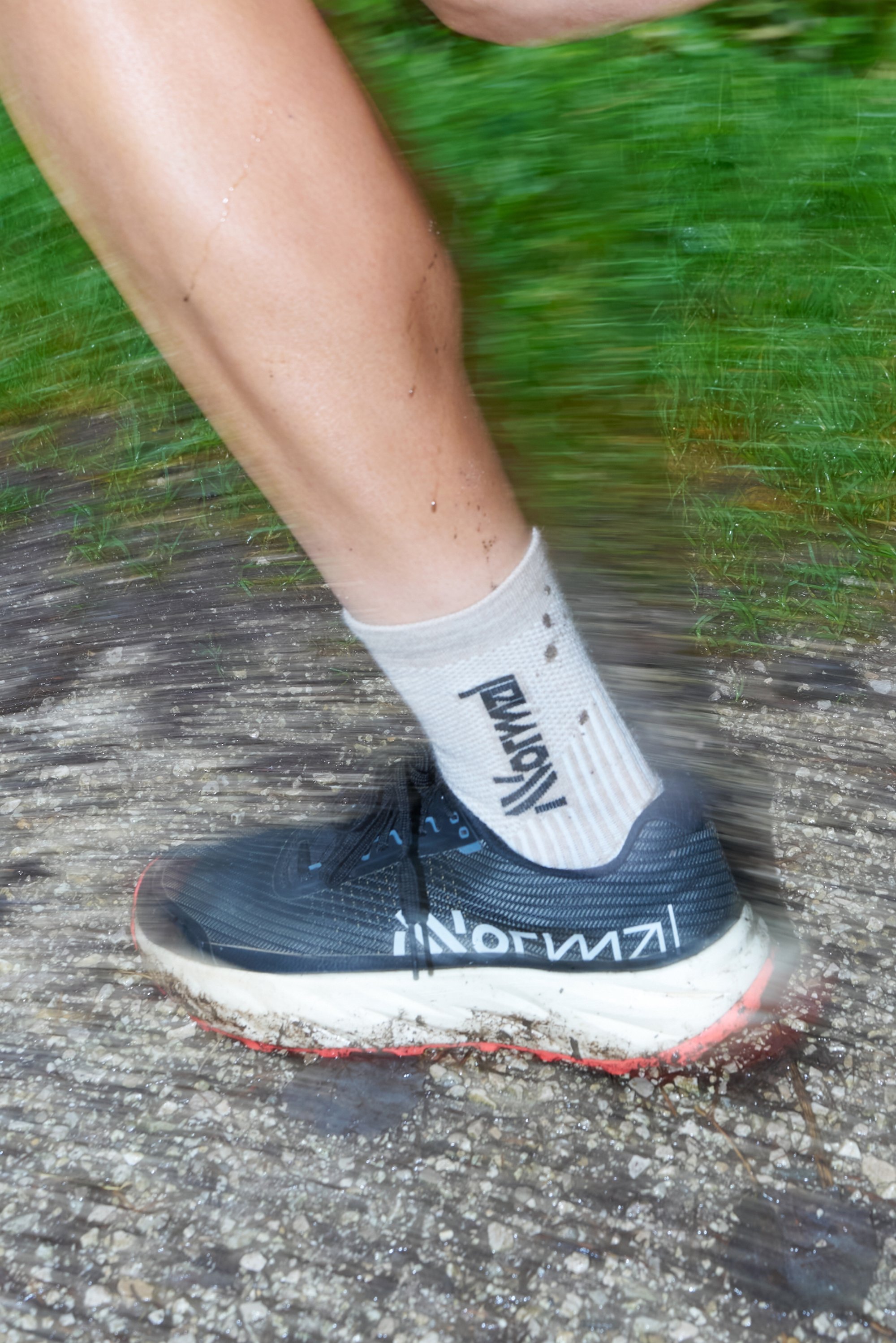 Black running shoe with white and red accents, textured surface, visible sole wear, and light grey sock displaying black text.